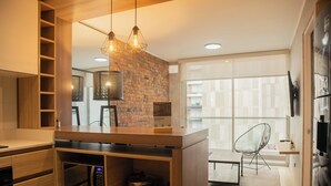 A modern kitchen with wooden cabinetry, a brick accent wall, and a dining area with a chair and table. - Exclusive Apartments in Pedro Martinto by Wynwood-House (Lima)