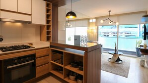 A modern kitchen with wooden cabinets, a gas stove, and a view of a marina through large windows. - Exclusive Apartments in Pedro Martinto by Wynwood-House (Lima)