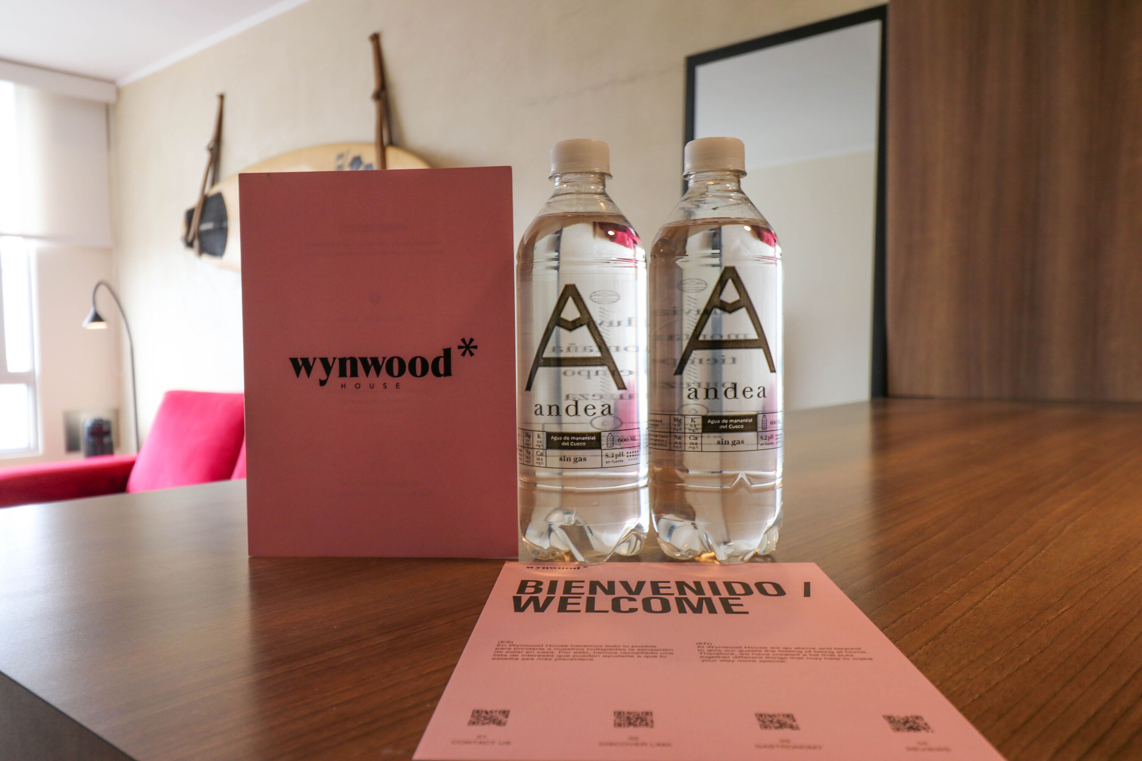 Een houten tafel met twee waterflessen, een roze welkomstkaart en een rode doos met de tekst 'wynwood* HOUSE'.