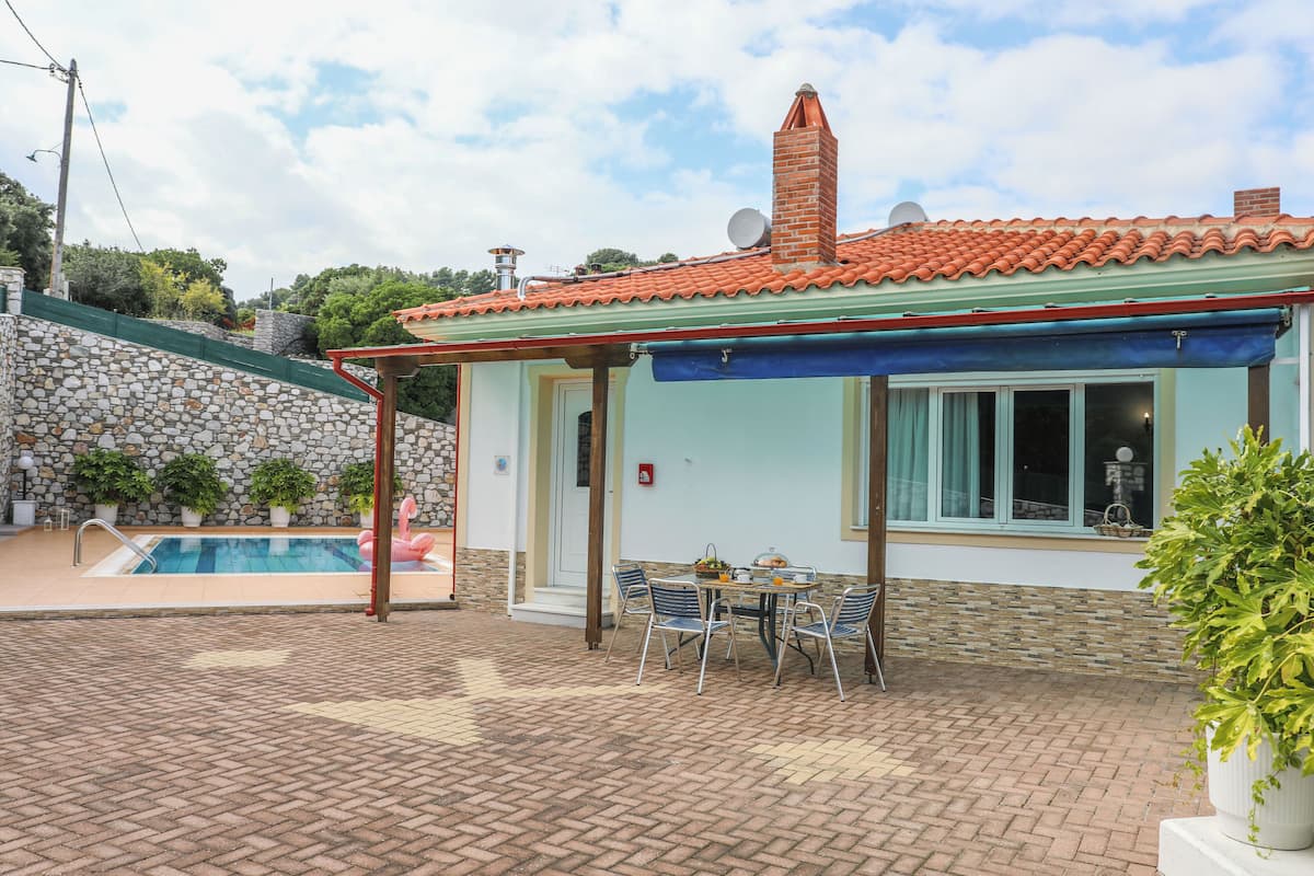 A house with a swimming pool, a patio with a table and chairs, and a brick wall.