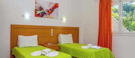 A hotel room with two beds, each with a green bedspread and white pillows, a wooden headboard, a painting on the wall, and a window with orange curtains.