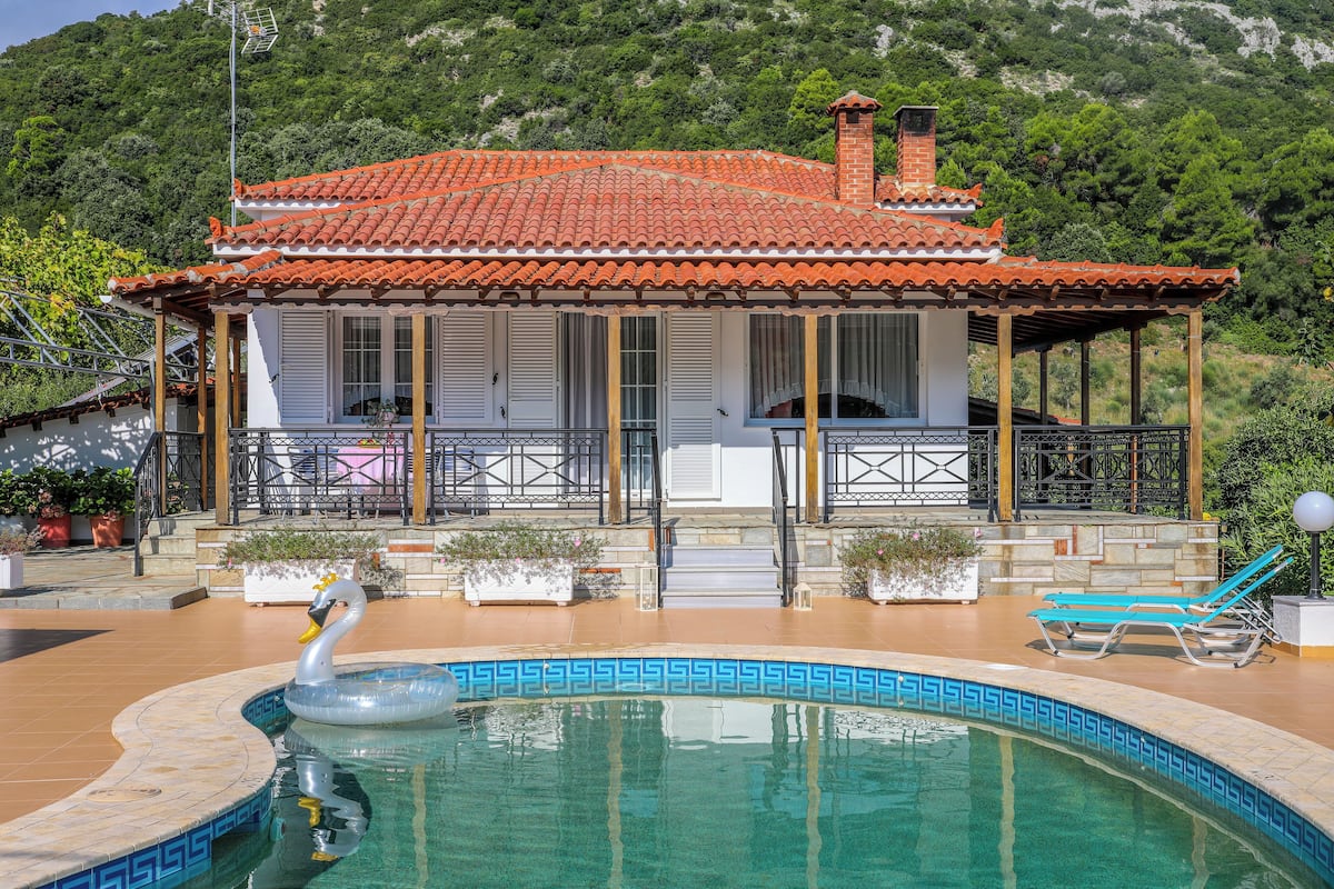 A villa with a swimming pool, a swan decoration, and a mountain backdrop.