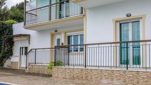 Un edificio de dos pisos con piscina, balcones con barandas de metal y fachada de piedra.