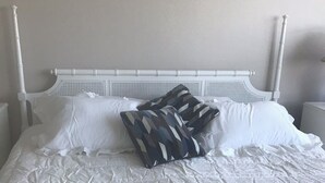 Un llit ben fet amb roba de llit blanca i almoinos amb dibuixos, un capçal de llit blanc i una paret senzilla.