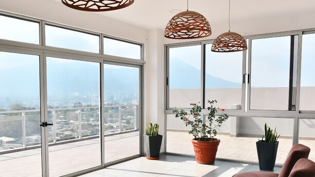 Varanda ampla com grandes janelas, plantas em vasos e luminárias pendentes.