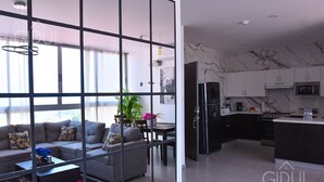 Um apartamento moderno com sala de estar, incluindo sofá, mesa de centro e área de jantar com mesa e cadeiras. A cozinha possui geladeira, micro-ondas e painel de fundo de mármore.