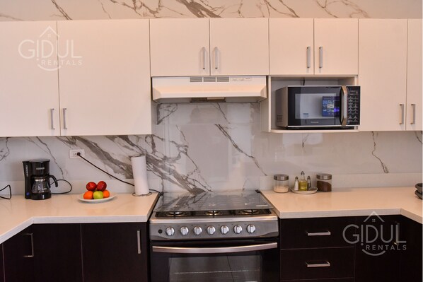 A kitchen with white cabinets, a black stove, a microwave, and a marble backsplash. - Prime Volcano Views Modern & Cozy Apartment (San Salvador)