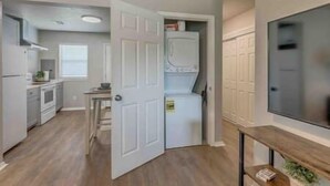 A compact kitchen with a built-in oven, a small dining area, and a laundry room with stacked washers and dryers. - 2-Bedroom Cottage w/ KING bed (Edmond)