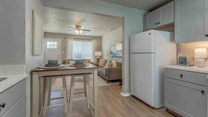 A compact kitchen with a refrigerator, a dining table with chairs, and a sofa in the adjacent living area. - 2-Bedroom Cottage w/ KING bed (Edmond)