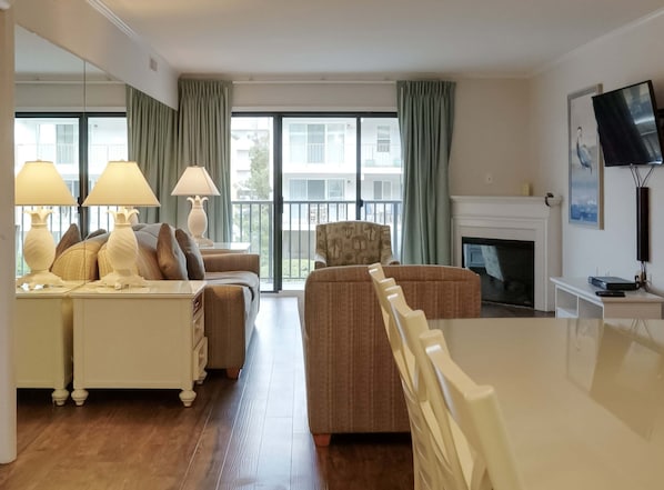 Habitación de hotel con sofá, mesa de comedor, chimenea y televisor en la pared.