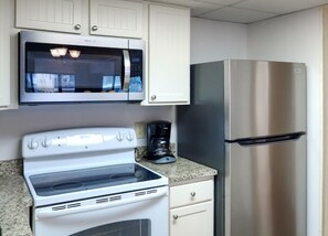 A kitchen with a microwave, stove, refrigerator, and coffee maker.