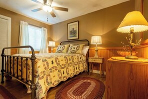 Ein Schlafzimmer mit Bett, Nachttisch, Lampe, Deckenventilator und einem gerahmten Bild an der Wand.