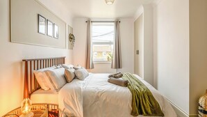 Un dormitorio ordenado con cama, lámpara de noche y ventana con cortinas.