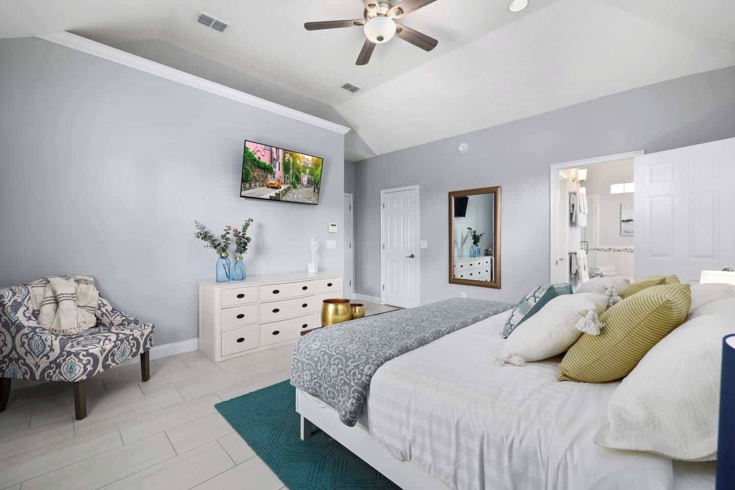A bedroom with a bed, a dresser, a chair, a TV, and a ceiling fan.