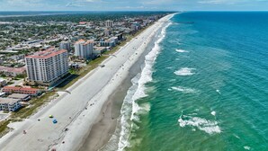 An aerial view of a coastal city with a long beach, high-rise buildings, and a pier extending into the ocean. - Family Beach Escape with Heated Pool & Games (Jacksonville Beach)