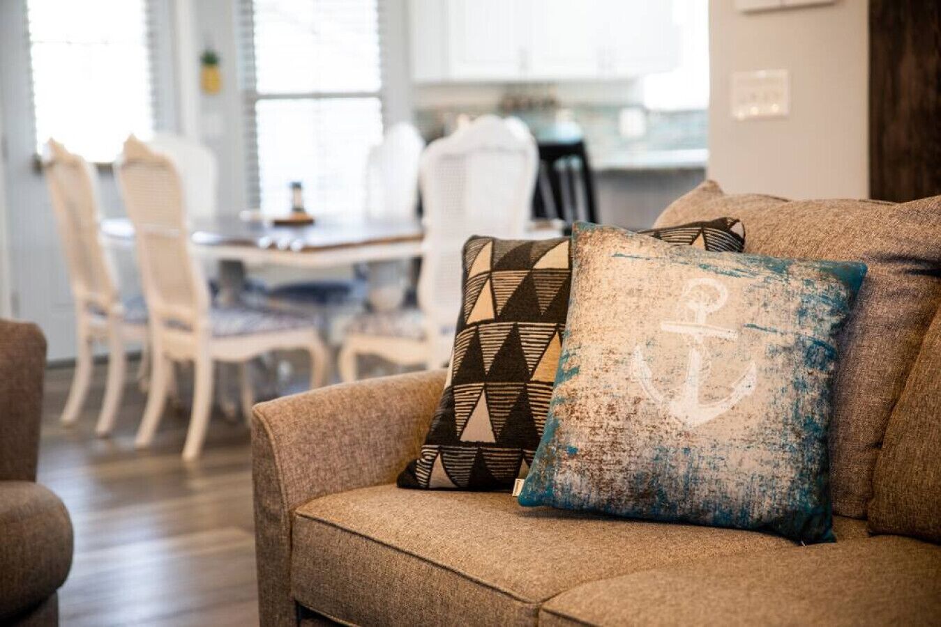 A living room with a sofa and patterned cushions, a dining area with chairs and a table, and a kitchen in the background.