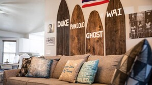 Un soggiorno con un divano marrone, cuscini decorativi e tavole da surf in legno con scritte sopra.