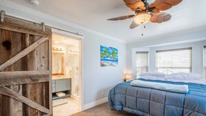 Una camera da letto con un letto, una ventola a soffitto, un quadro e una porta in legno.