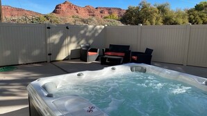 A hot tub with a view of red rock formations, a wooden deck, and outdoor furniture. - Gorgeous New Townhome with Hot Tub (Kanab)