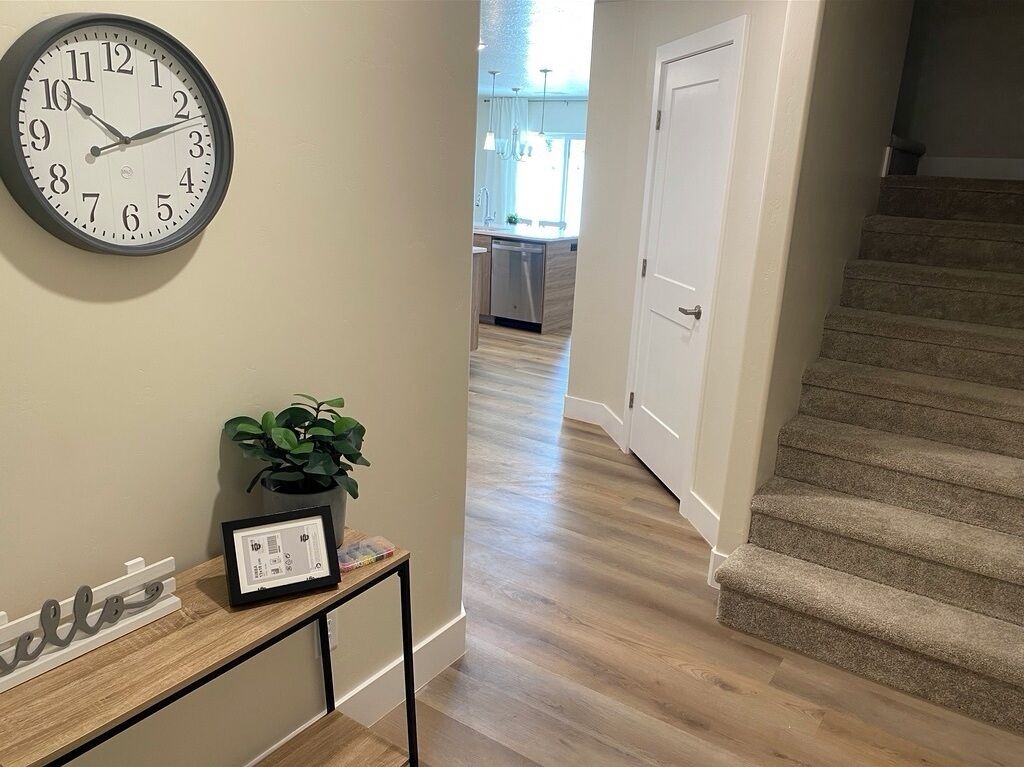 A hallway with a clock, a plant, and a framed certificate on a console table.