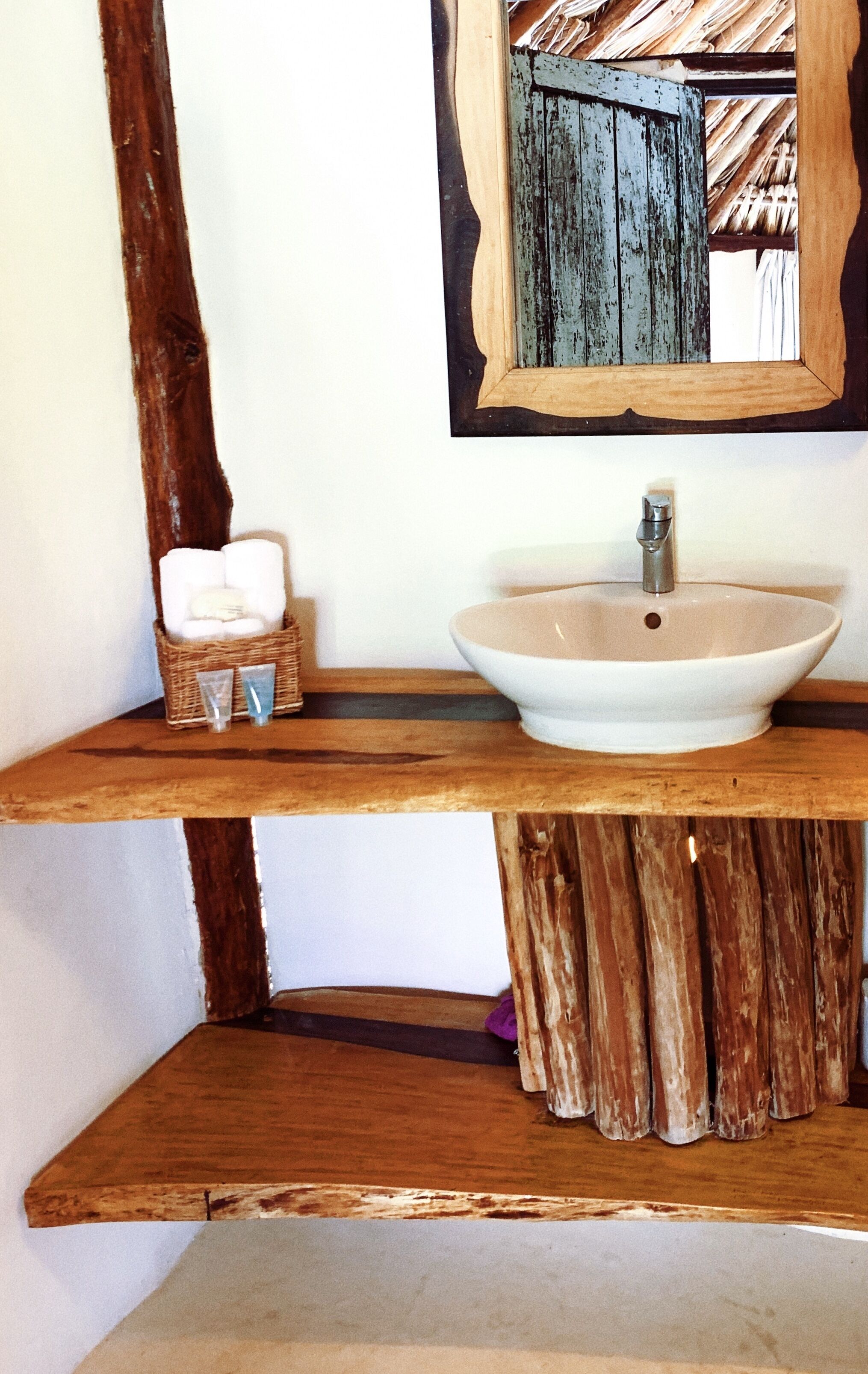 A bathroom with a wooden vanity, a white sink, and a mirror with a rustic frame.