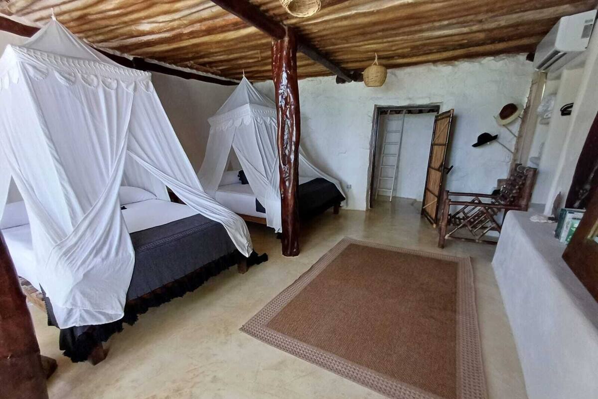A room with two beds covered in white canopy beds, a wooden table, and a small ladder against the wall.