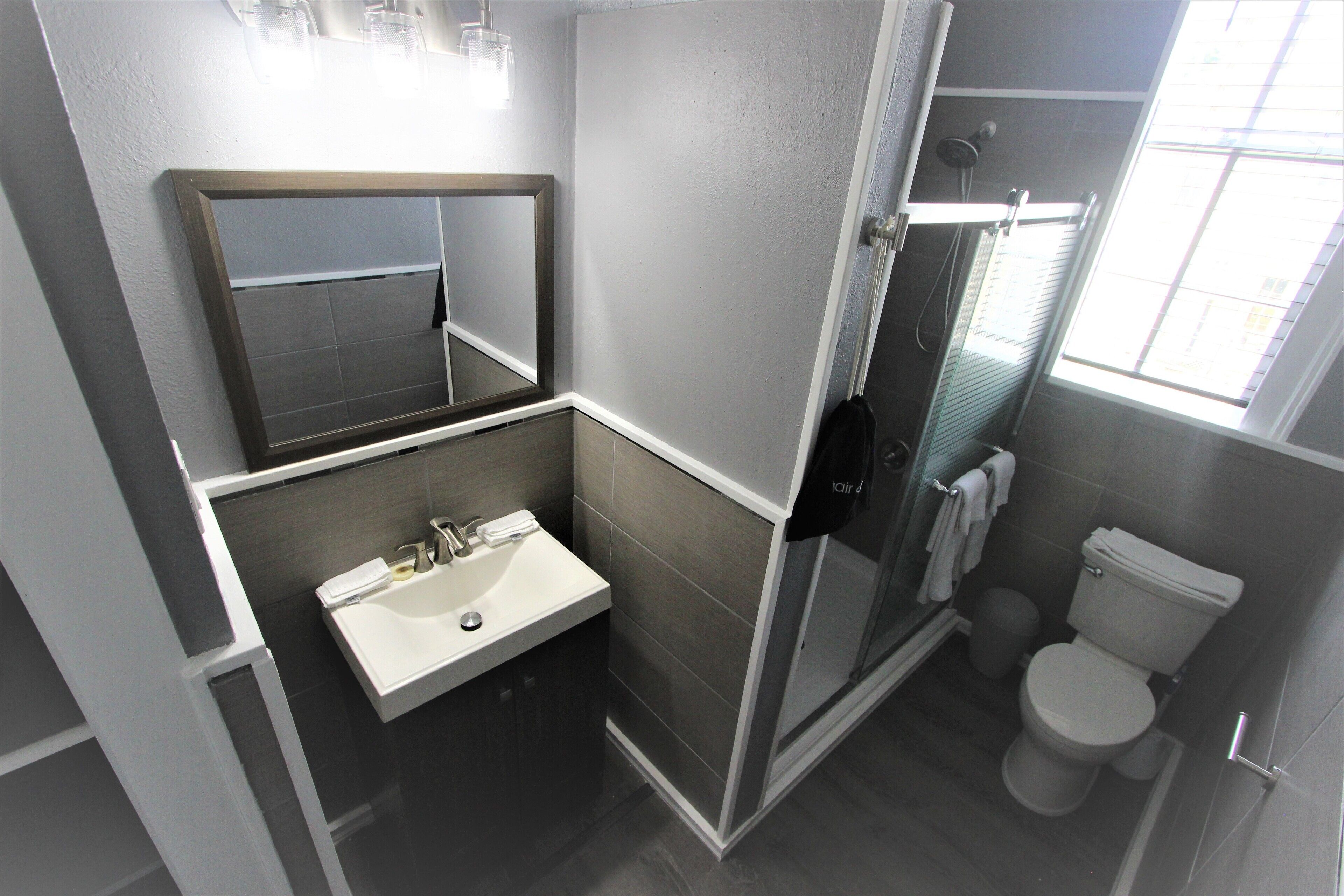Un baño moderno con un lavabo blanco, espejo e inodoro, y una cabina de ducha con mampara de vidrio.