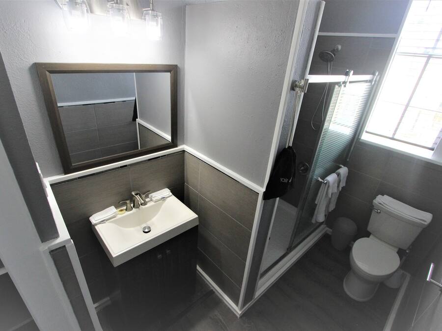 Un baño moderno con un lavabo blanco, espejo e inodoro, y una cabina de ducha con mampara de vidrio.