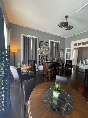 A dining area with a round table, chairs, a chessboard, a bar area with a wine rack, and a staircase leading to another level.