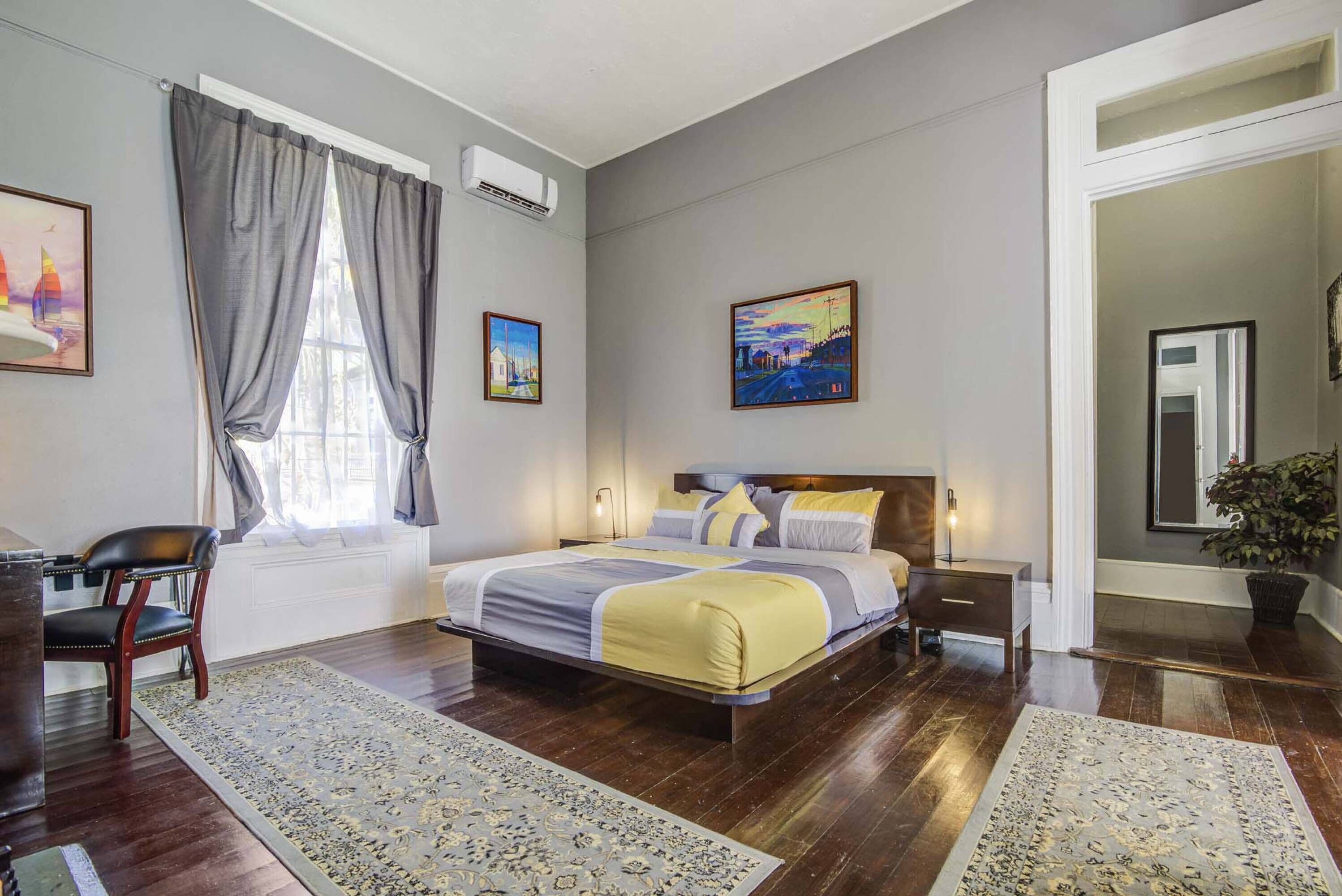 A bedroom with a large bed, a chair, a desk, and a window with curtains.