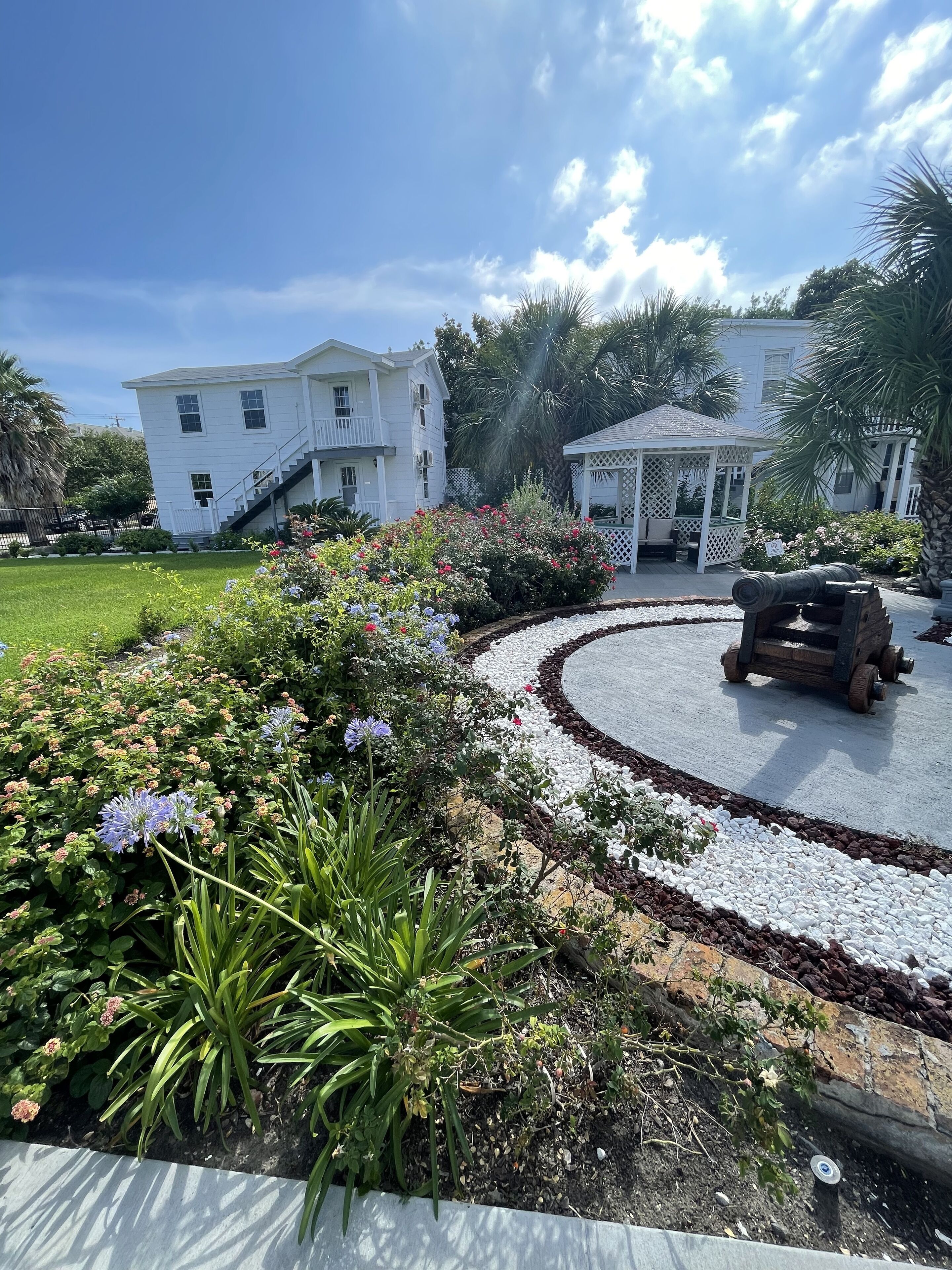 A white building with a porch and a gazebo in a landscaped garden.