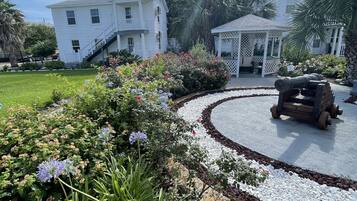 A white building with a porch and a gazebo in a landscaped garden.