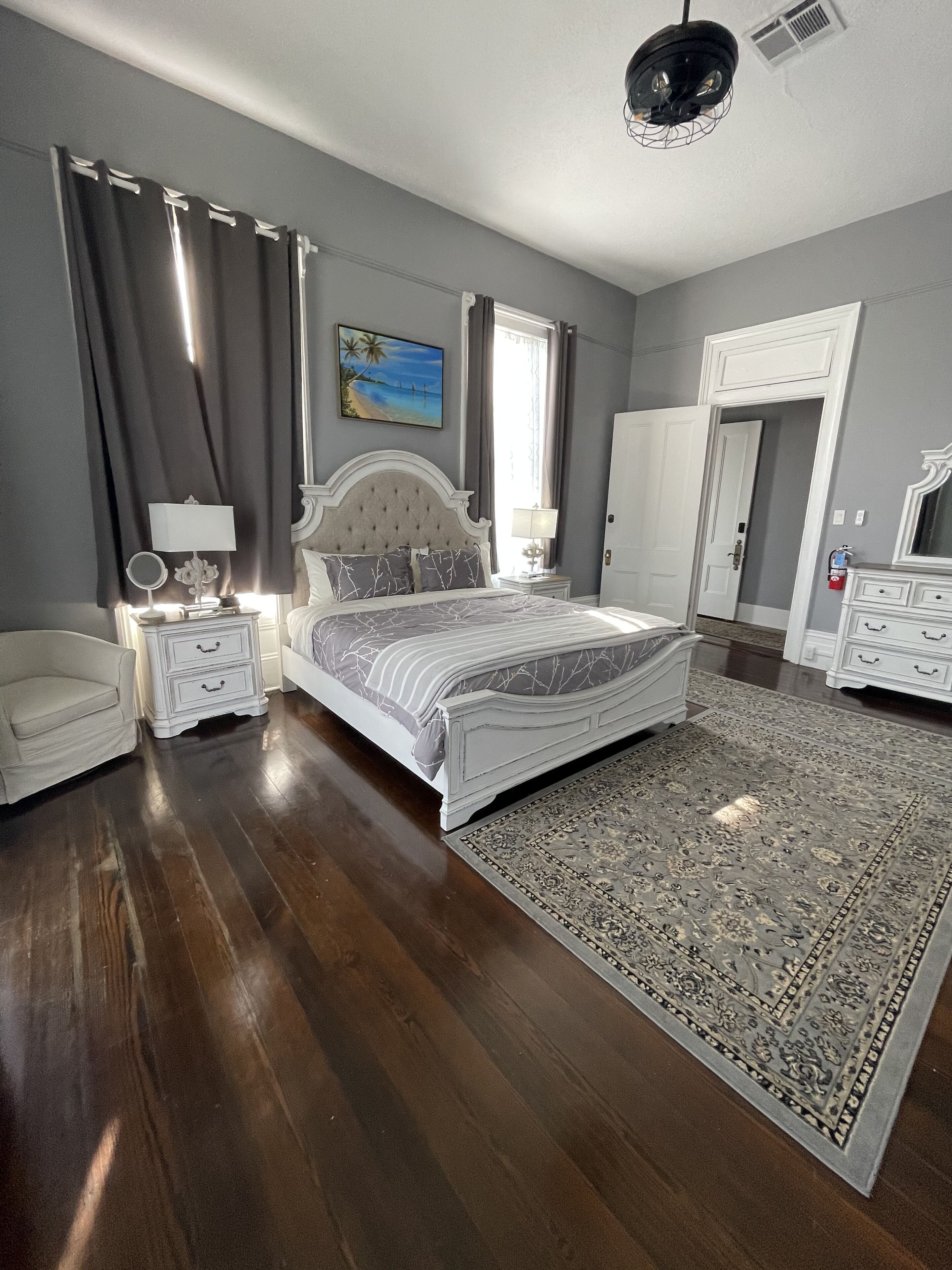 Une chambre à coucher avec un grand lit, une table de chevet avec une lampe, une commode, une chaise et un grand tapis.
