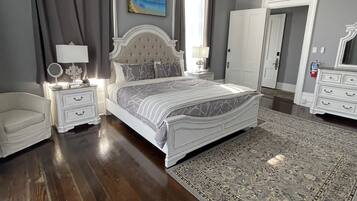 Une chambre à coucher avec un grand lit, une table de chevet avec une lampe, une commode, une chaise et un grand tapis.