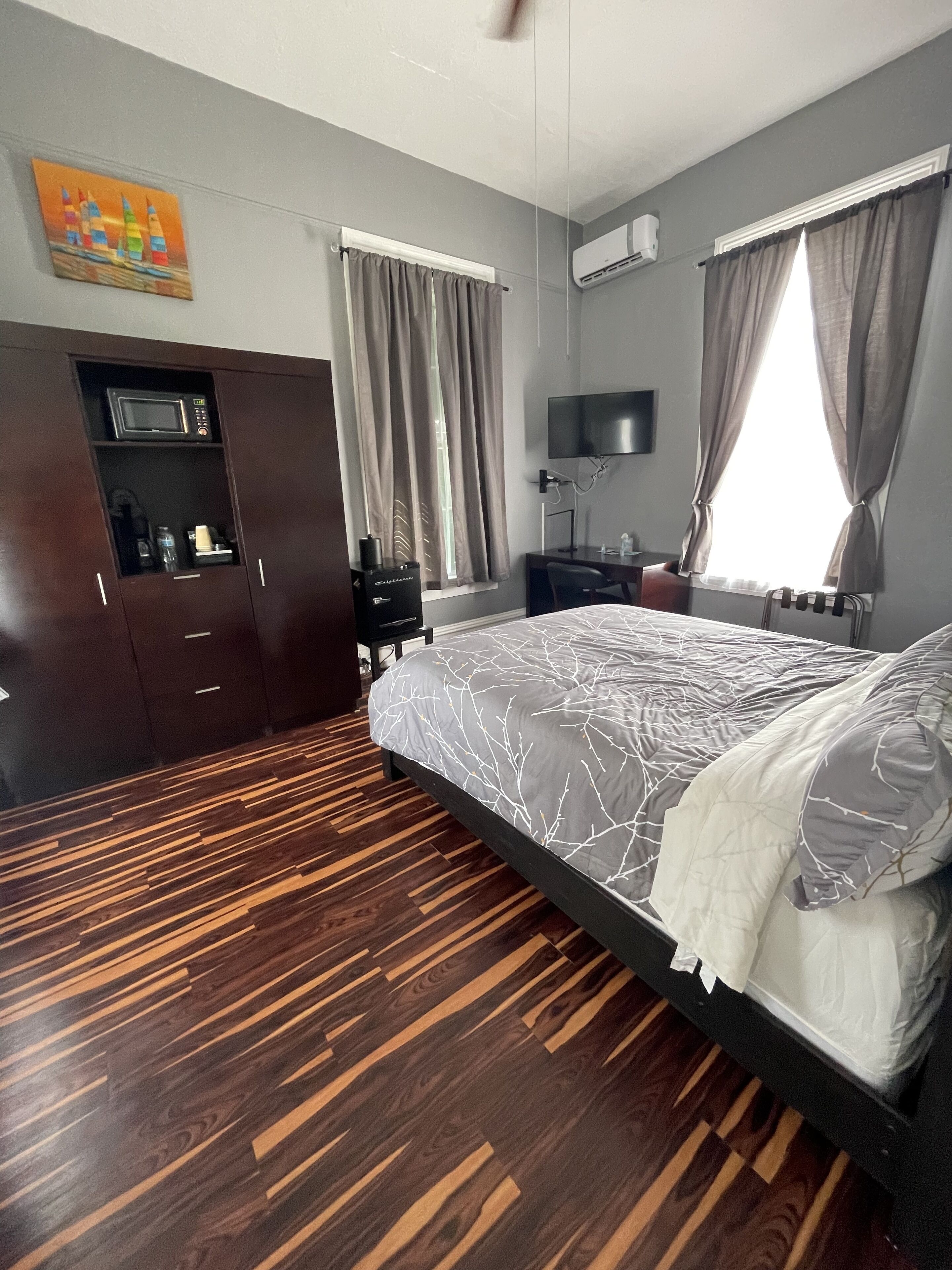 A bedroom with a bed, a desk, a TV, a wardrobe, and a window with curtains.
