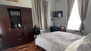 A bedroom with a bed, a desk, a TV, a wardrobe, and a window with curtains.