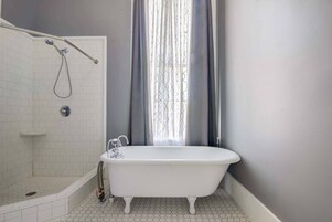 A bathroom with a freestanding bathtub, a shower, and a window with curtains.