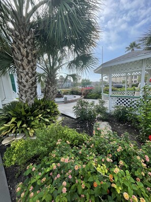 A garden with a gazebo, palm trees, and flowering plants. - The George Manor (Galveston)