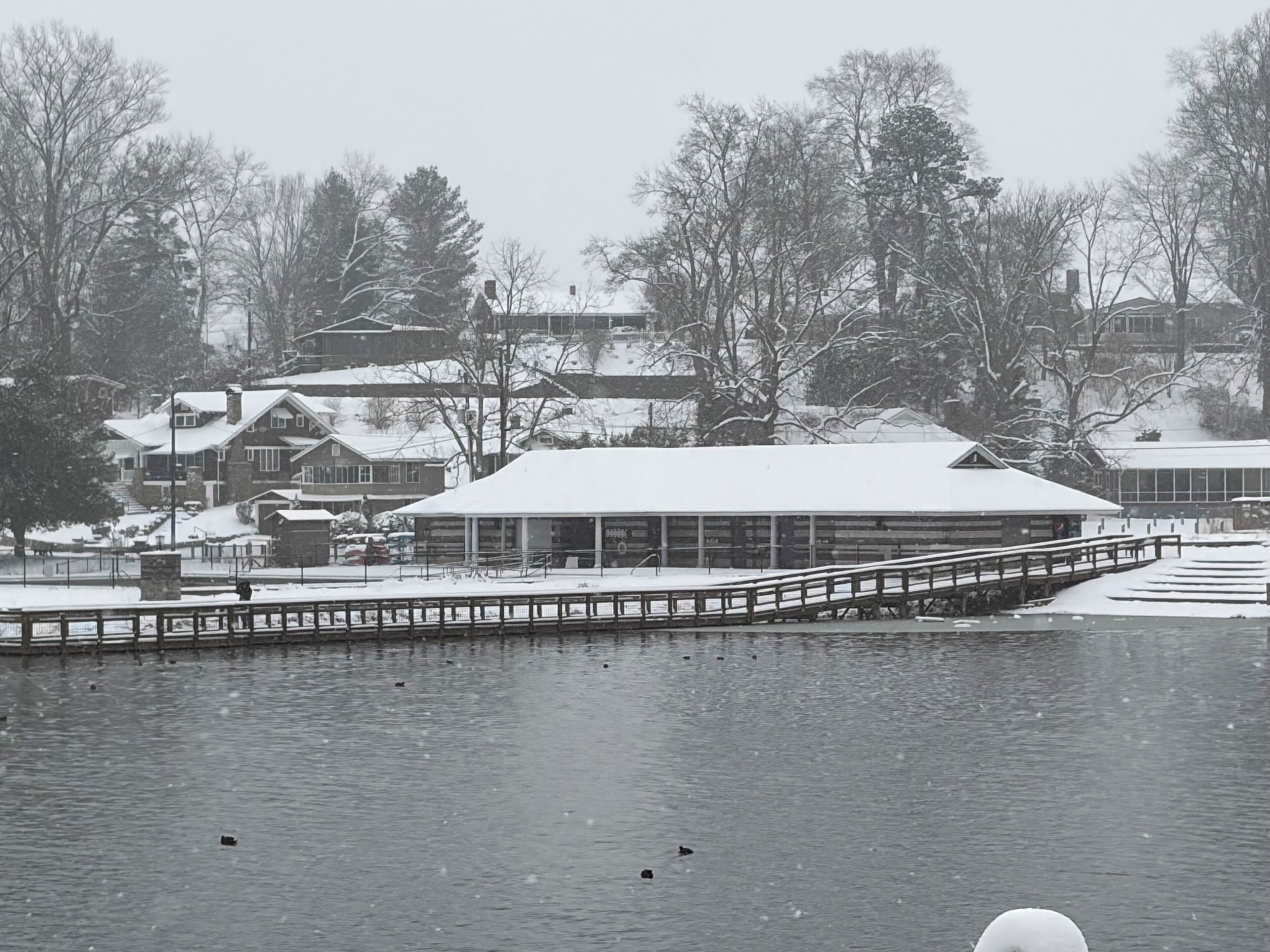 A snow-covered lakeside area with a dock extending into the water.