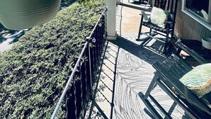 Une véranda avec un pot de fleurs suspendu, des sièges d’extérieur et une vue sur la maison.