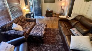 Un salon chaleureux avec un canapé à motifs, un divan en cuir et un téléviseur fixé au mur.