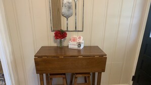Un bureau en bois, accompagné de deux tabourets assortis, se trouve dans une pièce dont le sol est recouvert de carreaux et où un miroir décoratif orne le mur.