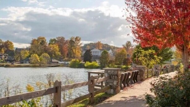 Une promenade au bord du lac, agrémentée d’une clôture en bois, de piliers en pierre et offrant une vue sur les maisons situées de l’autre côté de l’eau.