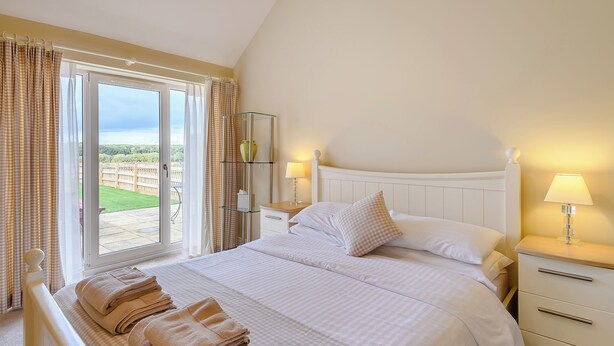 A bedroom with a bed, a bedside table, a lamp, a window with curtains, and a view of the outdoors. - The Parlour - UK36122 (Horsington)