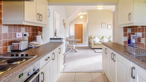 A modern kitchen with white cabinets, a built-in stove, and a dining area with a table and chairs. - The Parlour - UK36122 (Horsington)