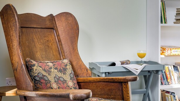 A wooden chair with a patterned cushion, a small table with a glass of orange juice, and a bookshelf with various books. - 2 bedroom accommodation in Crook, near Windermere (Crook, near Windermere)
