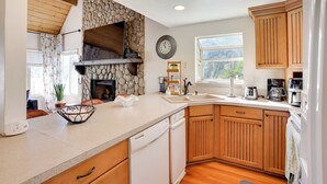 A kitchen with wooden cabinets, a stone wall, a clock, and a dishwasher. - Lake & Mountain-View Home: Walk to Downtown! (Crestline)