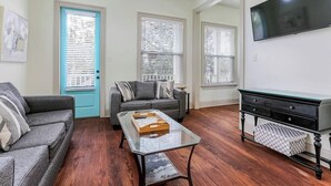 A living room with a sofa, a coffee table, a TV, and a door with blinds. - Chic NOLA Villa: Pet-Friendly, Patio & Fire Pit (New Orleans)