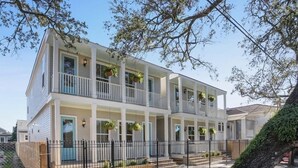 A two-story residential building with a balcony on each floor, a gated entrance, and a landscaped front yard. - Chic NOLA Villa: Pet-Friendly, Patio & Fire Pit (New Orleans)