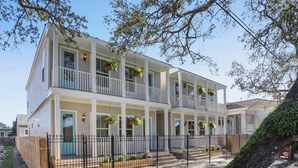 A two-story residential building with a balcony on each floor, a covered front porch, and a fenced front yard.
